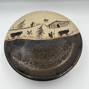 Assiette ronde motif poya avec vache, chalet, sapins et paysan sur 1 tiers de la surface